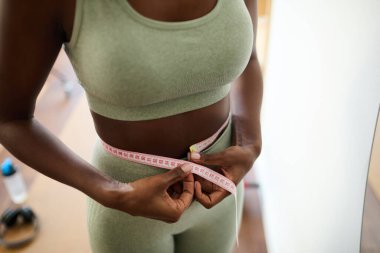 Kadının ölçüm bandıyla bel ölçümlerine yakın çekim, fitness ilerlemesini ve sağlıklı yaşam tarzını gösteriyor