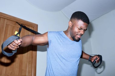 Afrika kökenli Amerikalı bir adam evde çalışmak için direniş bantları kullanıyor, fitness faaliyetlerinde kararlılık ve odaklanma gösteriyor