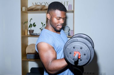 Siyah adam ağırlık çalışması için spor salonunda dambılı kaldırıyor ve biseps kıvrımına odaklanıyor.