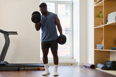 Afrika kökenli Amerikalı bir adam modern bir spor salonunda halterle biseps yapıyor.