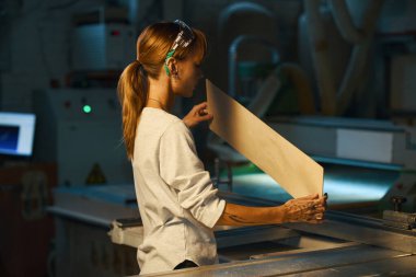 Genç kadın zanaatkar atölyedeki ahşabı torna tezgahında kesmeden önce inceliyor.