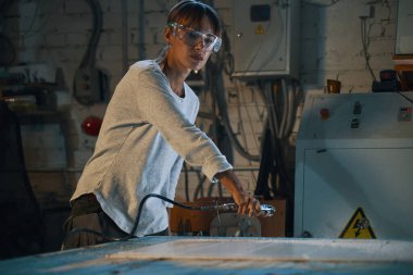 Koruyucu gözlüklü genç bir kadın özel ekipmanla üründen talaş topluyor.