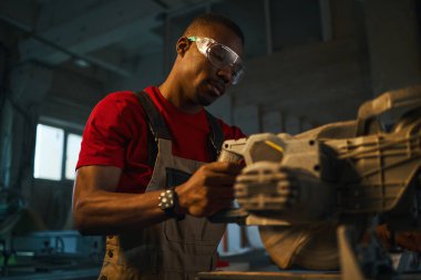 Koruyucu gözlüklü Afrikalı Amerikalı işçi fabrikada torna tezgahında çalışıyor.
