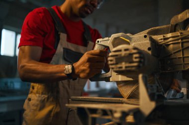 Afrikalı Amerikalı işçi atölyede testereyle çalışıyor.