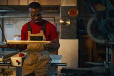 Makinede testereyle kestikten sonra ahşap ayrıntıları inceleyen işçiler