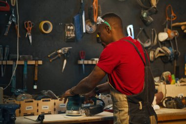 Afrika kökenli Amerikalı işçi atölyedeki masada makineyle tabela parlatıyor.