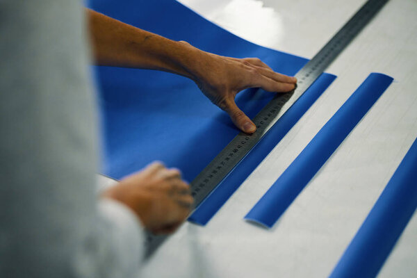 Высокоугол обзора рабочего с помощью линейки и резки красочных полос в мастерской