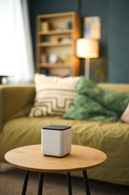Modern akıllı hoparlör yuvarlak ahşap masaya, çağdaş oturma odasının arka planına karşı, parlak tasarım ve işlevsellik ile dekorun geliştirilmesi