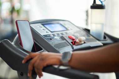 Yakından görüntü gösteren kadın spor yapıyor. Koşu bandı ve spor aleti kullanıyor. Arka plandaki su şişesine ve sapına odaklan.