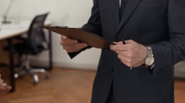 Tanımlanamayan çalışanın iş arkadaşına sözleşmeyi verirken ve ofis alanında el sıkışırken görüntüsü.