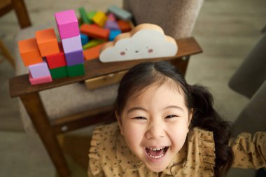 Kahkahalar atan genç bir kız rahat bir odada renkli tahta bloklarla oynayarak neşe ve çocukluk eğlencesi atmosferi yaratır.