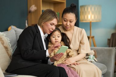 Kanepede teknoloji aygıtı üzerine üç kuşak aile bağı, akıllı telefondan küçük çocuklara ilginç içerikler gösteren yaşlı bir kadın.