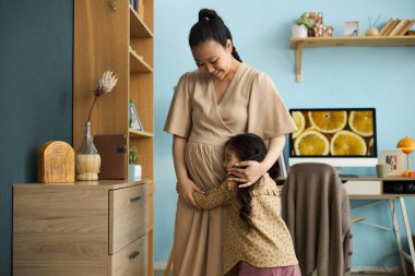 Asyalı bir anne, sıcak bir aile ortamı yaratmak için ev içinde mobilya ve dekorasyonlarla küçük kızına sarılıyor.