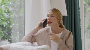 Evde cep telefonuyla konuşan beyaz bir kadının orta boy fotoğrafı.