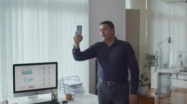 Modern ofis çalışma alanındaki cep telefonundan Asyalı erkek uzmanın orta boy görüntüsü.