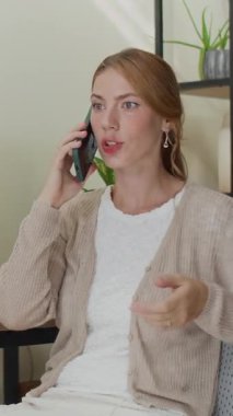 Beyaz kadın girişimcinin iş günü kapalı alanda akıllı telefondan konuşurken dikey görüntüsü.