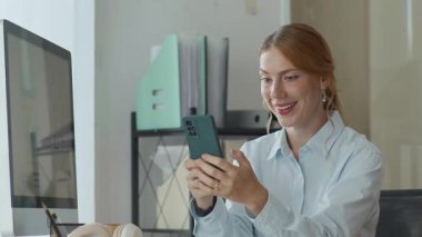 Ofiste cep telefonuyla mesajlaşırken resmi giyinen beyaz kadın yöneticinin orta boy fotoğrafı.