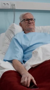 Kafkas erkek hastanın hastane koğuşunda yatağında dinlenirken kameraya baktığı dikey portre fotoğrafı.