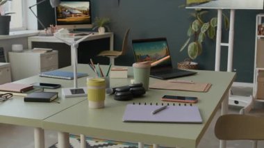 Açık dizüstü bilgisayarlı ortak ofis masası, yeniden kullanılabilir kahve fincanları, not defterleri, rüzgar türbini modeli ve modern çalışma alanındaki akıllı telefonlar.