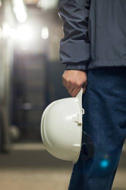 Tanımlanamayan erkek müteahhidin dikey görüntüsü. Hareketsiz duruyor ve elinde beyaz plastik kasketle.