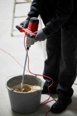 Tanımlanamayan erkek işçinin dikey çekimi. Matkap yardımıyla çimentoyu karıştırıyor.