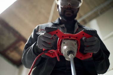 Betonu harmanlarken elinde elektrikli matkap tutan Afrikalı Amerikalı adamın düşük açılı görüntüsü.