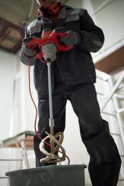 Profesyonel işçinin elindeki düşük açılı kirli matkap mikseri, onu çimento dolu kirli plastik kovadan alıyor.
