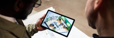 Tablet ekran tanıtım ofis planına bakan çift ırklı mimarların yer aldığı bir web sitesi afişi