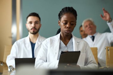 Dijital tabletler üzerinde hasta verilerinin incelenmesi ve tıbbi vakaların tartışılması gibi önemli bir toplantıda işbirliği yapan çeşitli tıbbi ekiplerin portresi