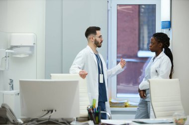 İki doktor modern bir ofiste, pencere kenarında tıbbi bir durumu tartışıyorlar. Hem ciddi hem de konuşma üzerine odaklanmışlar. Arka planda çeşitli tıbbi cihazlar var.