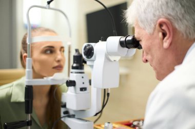 Göz muayenesi sırasında ileri tıbbi ekipman kullanan yaşlı bir erkek doktor gözlerini kontrol ettiriyor.
