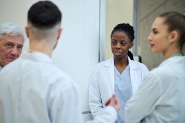 Çok ırklı bir grup doktor hastanede hasta tedavi planını tartışıyor. Ekipte kıdemli doktor ve tıp üniformalı genç profesyoneller de yer alıyor.