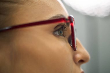 İnsan gözüne odaklanmış kırmızı gözlük takıyor ve derin düşüncelere dalmış bir anı yakalıyor.