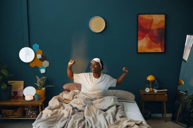 Güzel dekore edilmiş, duvarları ve bitkileri olan bir odada uzanan gülümseyen bir kadın. Yatak odasının modern dekorasyonu ve sıcak atmosferi var.