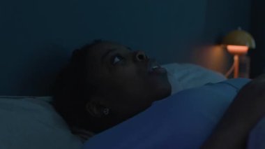 Genç Afrikalı Amerikalı kadın karanlık odada uyuyor, kabus görüyor ve korku içinde uyanıyor.