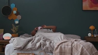 Genç siyahi kadın uyanıyor, uyku maskesini çıkarıyor, yatakta oturuyor ve sabahın erken saatlerinde kendini evinde hissediyor.