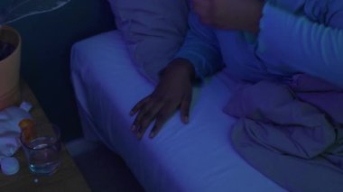 Genç siyahi kadın haplar alıyor, su içiyor ve geceleri karanlık odada yatağında uyuyor.