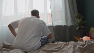 Pijamalı, kahve içen ve gününü evde geçirirken pencereden bakan yaşlı adamın dikiz aynası.