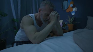 Başı eğik ve elleri bağlı olarak yatağın başında oturan Kafkasyalı kıdemli bir adam gece evde uyumadan önce Tanrı 'ya dua ediyor.