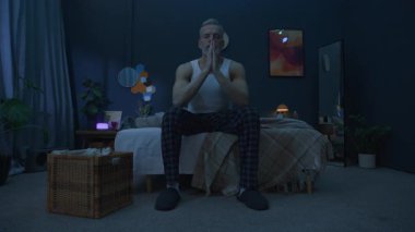 Son sınıf öğrencisi yatağın kenarında oturmuş, geceleri rahat ve loş bir odada uyumadan önce ellerini sımsıkı bağlayıp dua ediyor.