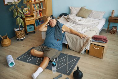 Orta yaşlı bir adam egzersiz malzemesi ve ev dekoruyla çevrili, rahat yatak odası döşeğinde spor yapıyor.