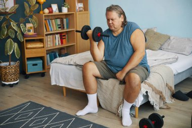 Oturma odasındaki kanepenin kenarına oturan bir adam belli ki azim ve çabayla egzersiz rutinine odaklanmış görünüyor.