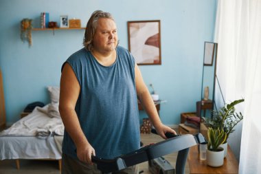 Arka planda bitkiler ve duvar sanatı ile koşu bandında egzersiz yapan orta yaşlı beyaz adamın portresi