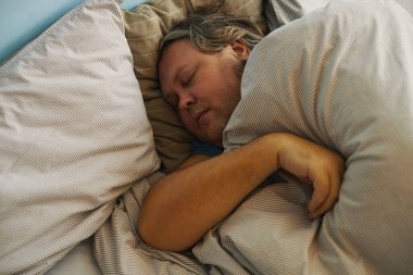 Huzurlu bir şekilde uyuyan, çizgili bir yatak, sakin bir yüz ifadesi sergileyen bir adam.