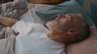 Beyaz tişörtlü, rahat bir yatakta uyuyan son sınıf öğrencisinin yakın görüntüsü.