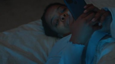 Uykusuzluk çeken Afrika kökenli Amerikalı bir kadın karanlık odada yatağında uzanıyor, uykusuz bir gecede cep telefonuyla kayıyor.