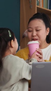 Evde dizüstü bilgisayarda çalışan genç bir çocuğun içki içtiği dikey bir fotoğraf.