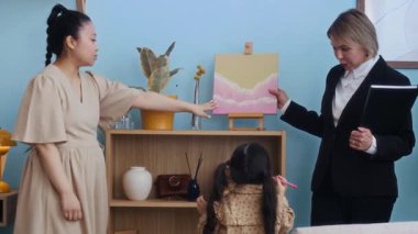 Genç hamile bir kadın ve sosyal hizmetler görevlisinin modern tablonun yanında durup, randevusu sırasında küçük bir kızla konuştuğu orta boy bir fotoğraf.