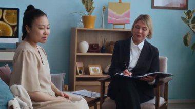 Orta yaşlı, Asyalı bir annenin, evini ziyaret ederken orta yaşlı bir kadın sosyal hizmet görevlisiyle konuşurken orta ölçekli bir görüntüsü.