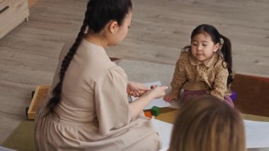 Kadın sosyal hizmet görevlisinin kağıt doldurma ziyareti sırasında küçük kızının resim çizmesine yardım eden Asyalı bir annenin aşağı eğilmiş görüntüsü.